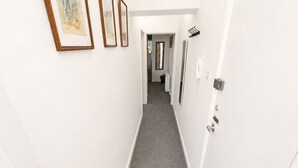 A narrow hallway with a carpeted floor, white walls, and framed artwork. - Free Parking | Homely Gloucester Rd Flat Sleeps 3 (Bristol)
