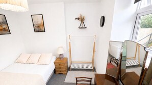 A bedroom with a bed, bedside table, lamp, wooden wardrobe, mirror, and a window with a view. - Free Parking | Homely Gloucester Rd Flat Sleeps 3 (Bristol)