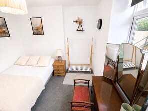 Ein Schlafzimmer mit Bett, Nachttisch, Lampe, Holzschrank, Spiegel und einem Fenster mit Ausblick.