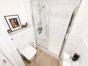 Ein modernes Badezimmer mit Duschkabine aus Glas, Toilette, Waschbecken und einem gerahmten Bild an der Wand.