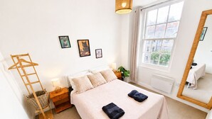 Quarto bem arrumado com cama, mesas de cabeceira, uma cadeira suspensa e uma janela grande.