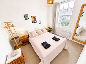 Ein ordentlich eingerichtetes Schlafzimmer mit einem Bett, Nachttischen, einem Hängekorbsessel und einem großen Fenster.