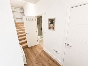 Ein Flur mit Holzboden, einer weißen Tür, einer Glasdusche und einem an der Wand montierten Lichtschalter.