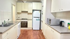 Uma cozinha compacta com armários brancos, forno embutido, geladeira e micro-ondas.