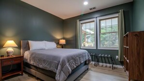 A bedroom with a bed, two bedside lamps, a radiator, and a window with curtains.