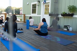 A group of people on yoga mats on a wooden deck with a building in the background.