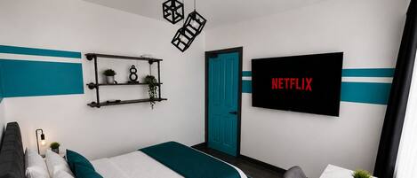 A modern bedroom with a bed, desk, TV, and decorative items.