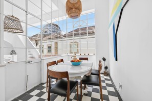 Ein Essbereich mit einem weißen Tisch, einem schwarz-weißen Schachbrettfußboden und Blick auf Gebäude durch große Fenster.