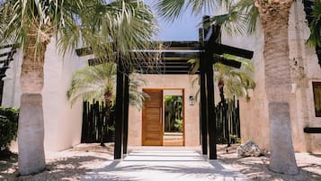 Un sendero que conduce a una puerta de madera, con vista a un jardín y palmeras.