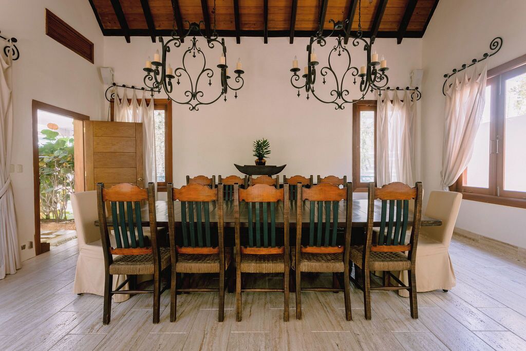 A dining area with a wooden table and chairs, a chandelier, and a view through a window.