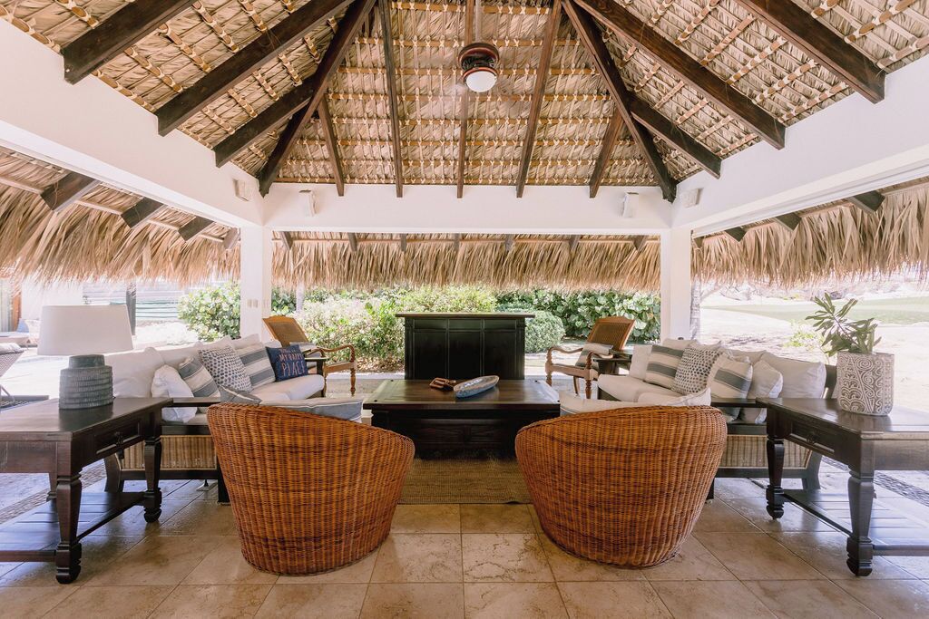 An open-plan living area with a thatched roof, wicker furniture, and a fireplace.