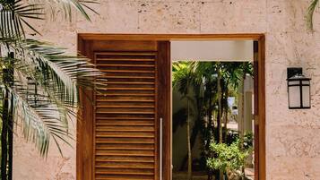 A wooden door with a glass panel, leading to a courtyard with palm trees and a tiled floor.