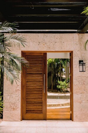 Una puerta de madera con un panel de vidrio que da a un patio con palmeras y piso de baldosas.