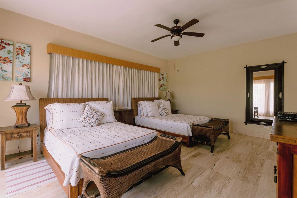 A bedroom with two beds, a ceiling fan, a window with curtains, and a mirror on the wall.