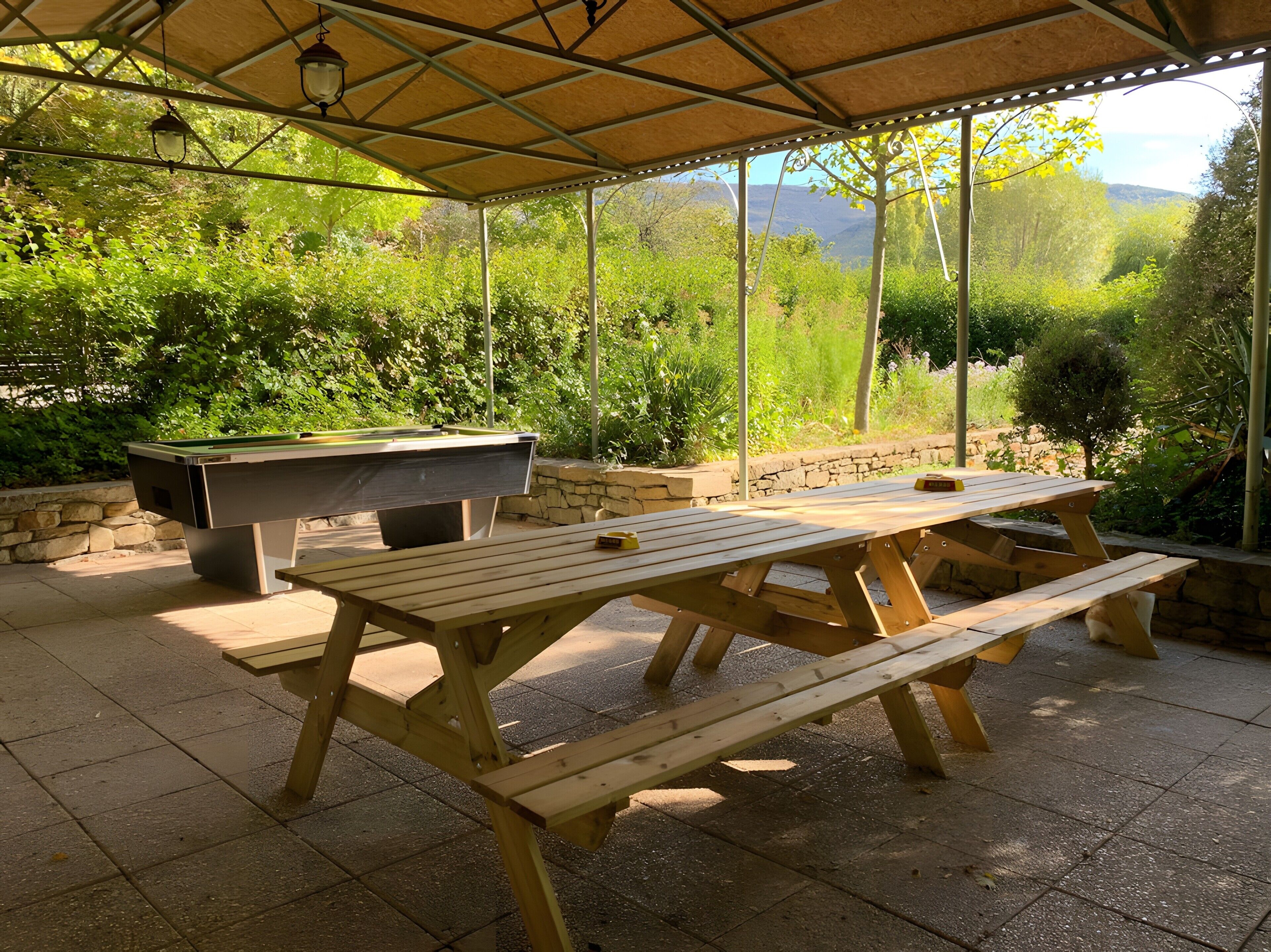 An outdoor patio with a pool table, wooden benches, and a stone wall.