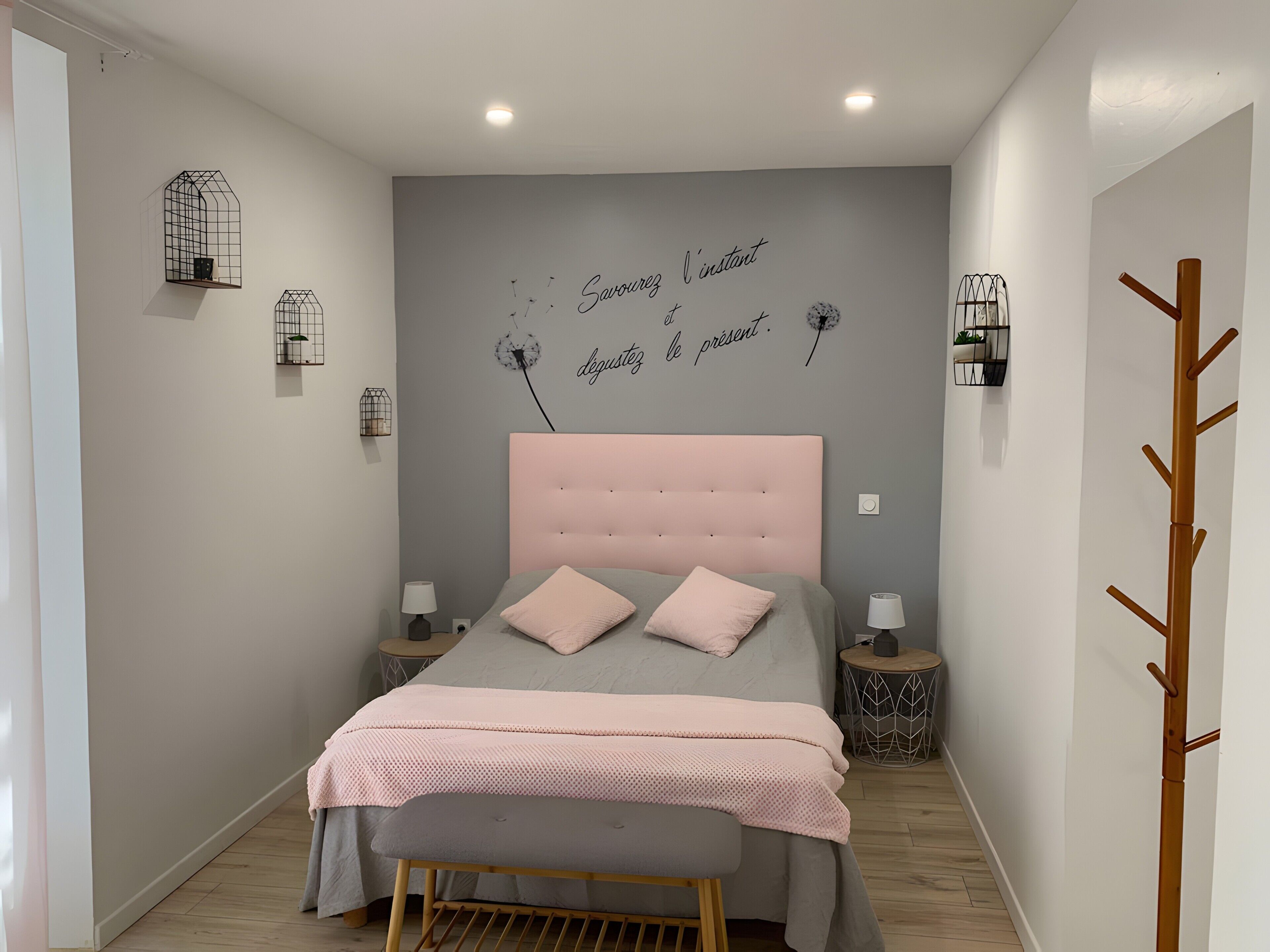 A bedroom with a bed, bedside tables, wall decor, and a wooden coat rack.