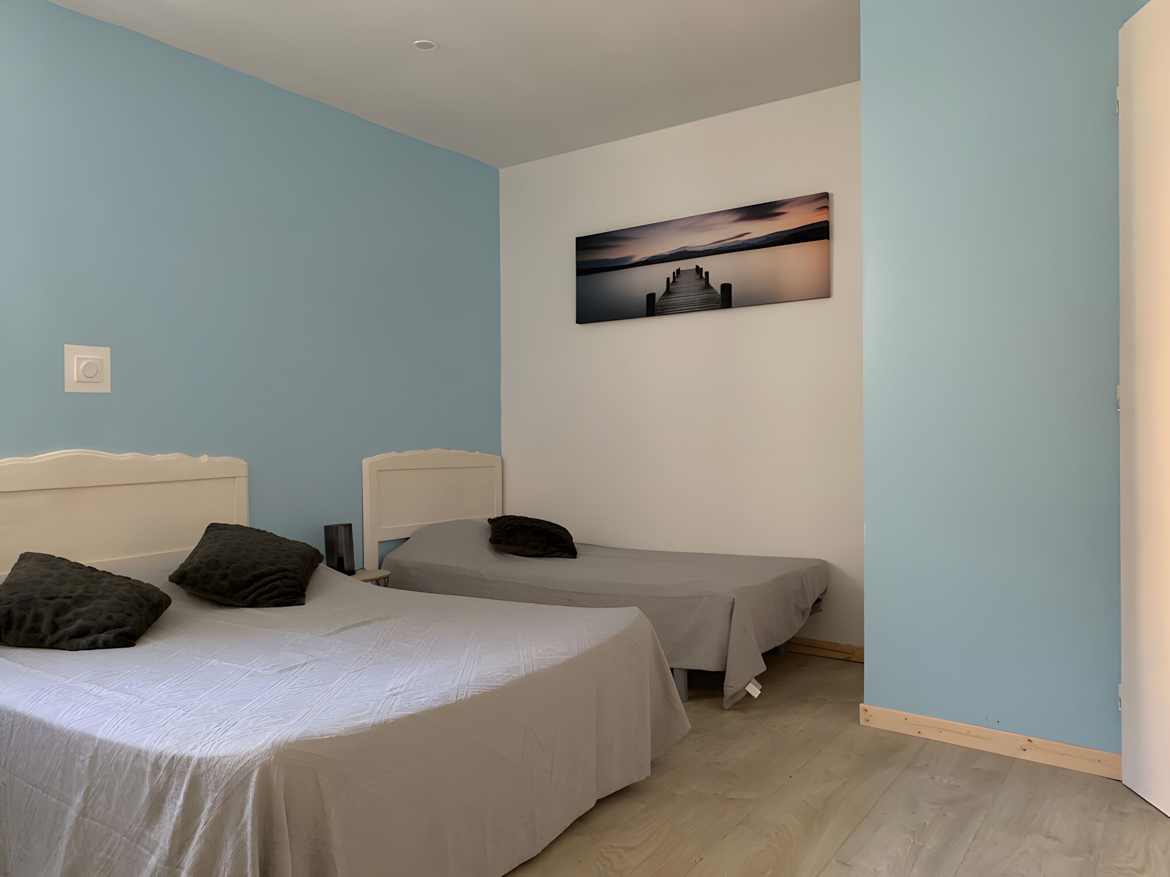 Une chambre avec deux lits simples, un tableau au mur et un interrupteur sur le mur.