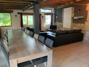 Een ruime kamer met een lange eettafel, een bank en een stenen openhaard.