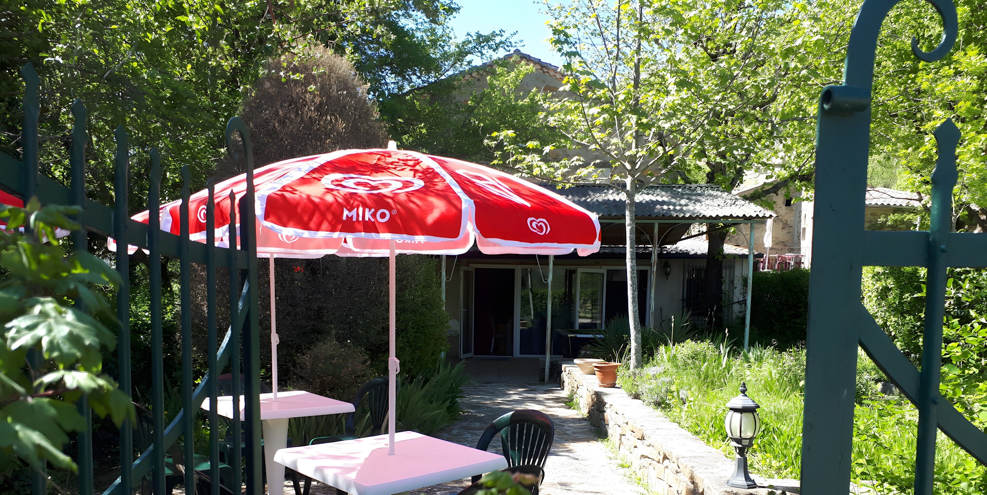 An outdoor seating area with a red and white umbrella, a stone pathway, and greenery.