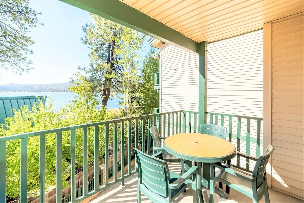 A balcony with a table and chairs, overlooking a body of water and trees.