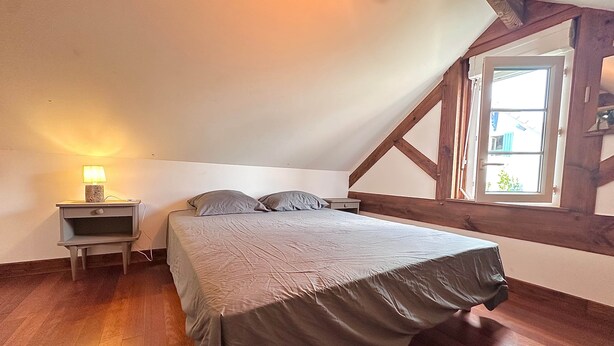 A bedroom with a bed, nightstands, a lamp, wooden beams, and a window. - Air Salin - 3-Bedroom House 50 Meters from the Ocean (Mimizan)