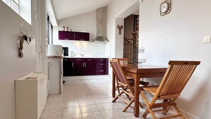 A kitchen with dark cabinets, a dining table with wooden chairs, and a clock on the wall. - Air Salin - 3-Bedroom House 50 Meters from the Ocean (Mimizan)