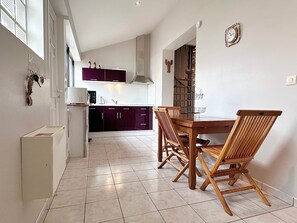 A kitchen with dark cabinets, a dining table with wooden chairs, and a clock on the wall. - Air Salin - 3-Bedroom House 50 Meters from the Ocean (Mimizan)