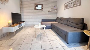 A living room with a TV, a sofa, a coffee table, and a wall-mounted shelf. - Air Salin - 3-Bedroom House 50 Meters from the Ocean (Mimizan)