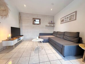 A living room with a TV, a sofa, a coffee table, and a wall-mounted shelf. - Air Salin - 3-Bedroom House 50 Meters from the Ocean (Mimizan)