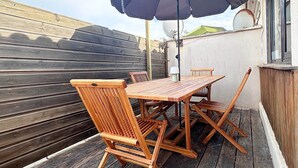 A wooden deck with a table and chairs, an umbrella, and a wall with a satellite dish. - Air Salin - 3-Bedroom House 50 Meters from the Ocean (Mimizan)