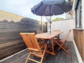 A wooden deck with a table and chairs, an umbrella, and a wall with a satellite dish. - Air Salin - 3-Bedroom House 50 Meters from the Ocean (Mimizan)