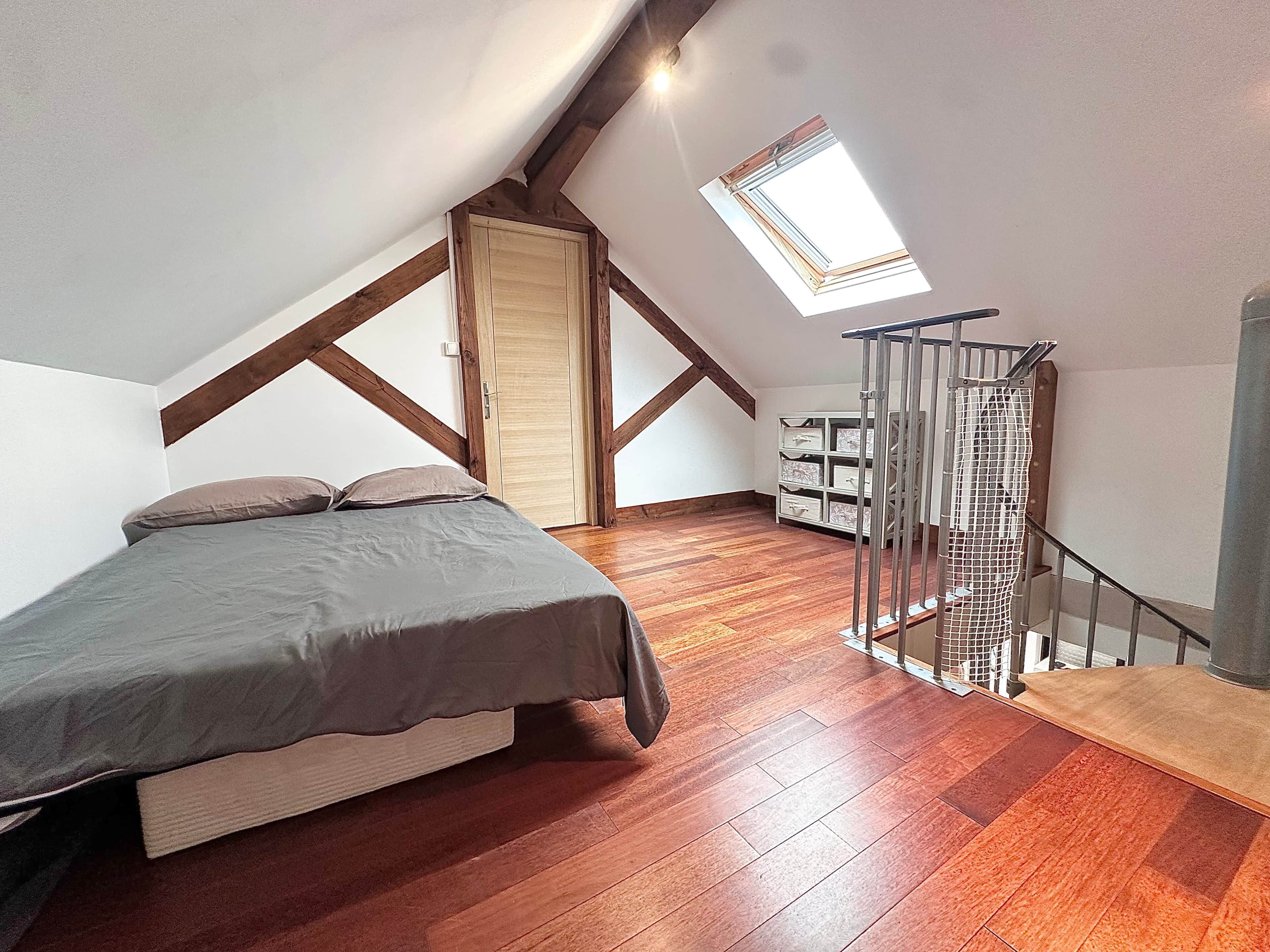 Un dormitorio con techo inclinado, tragaluz, cama, suelo de madera y una escalera con barandilla.