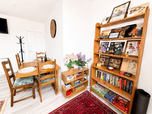 Ein Essbereich mit einem Holztisch und Stühlen, einem Bücherregal mit Büchern und gerahmten Bildern sowie einem Teppich mit rotem Muster.