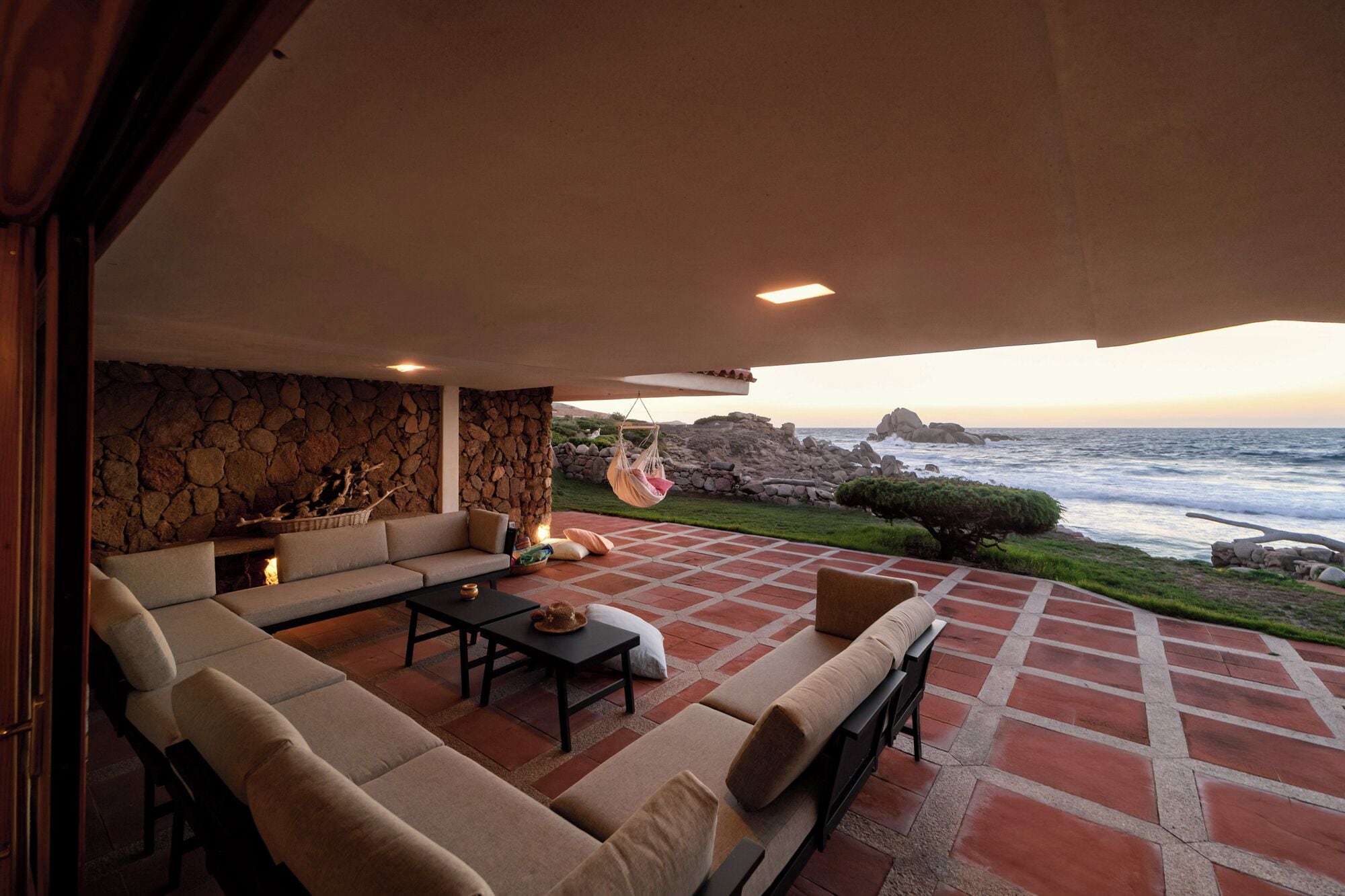 A cozy outdoor seating area with a stone wall, a hanging chair, and a view of the ocean.