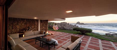 A cozy outdoor seating area with a stone wall, a hanging chair, and a view of the ocean.