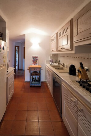 Uma cozinha com armários brancos, piso ladrilhado, bancada com cafeteira e porta-facas.