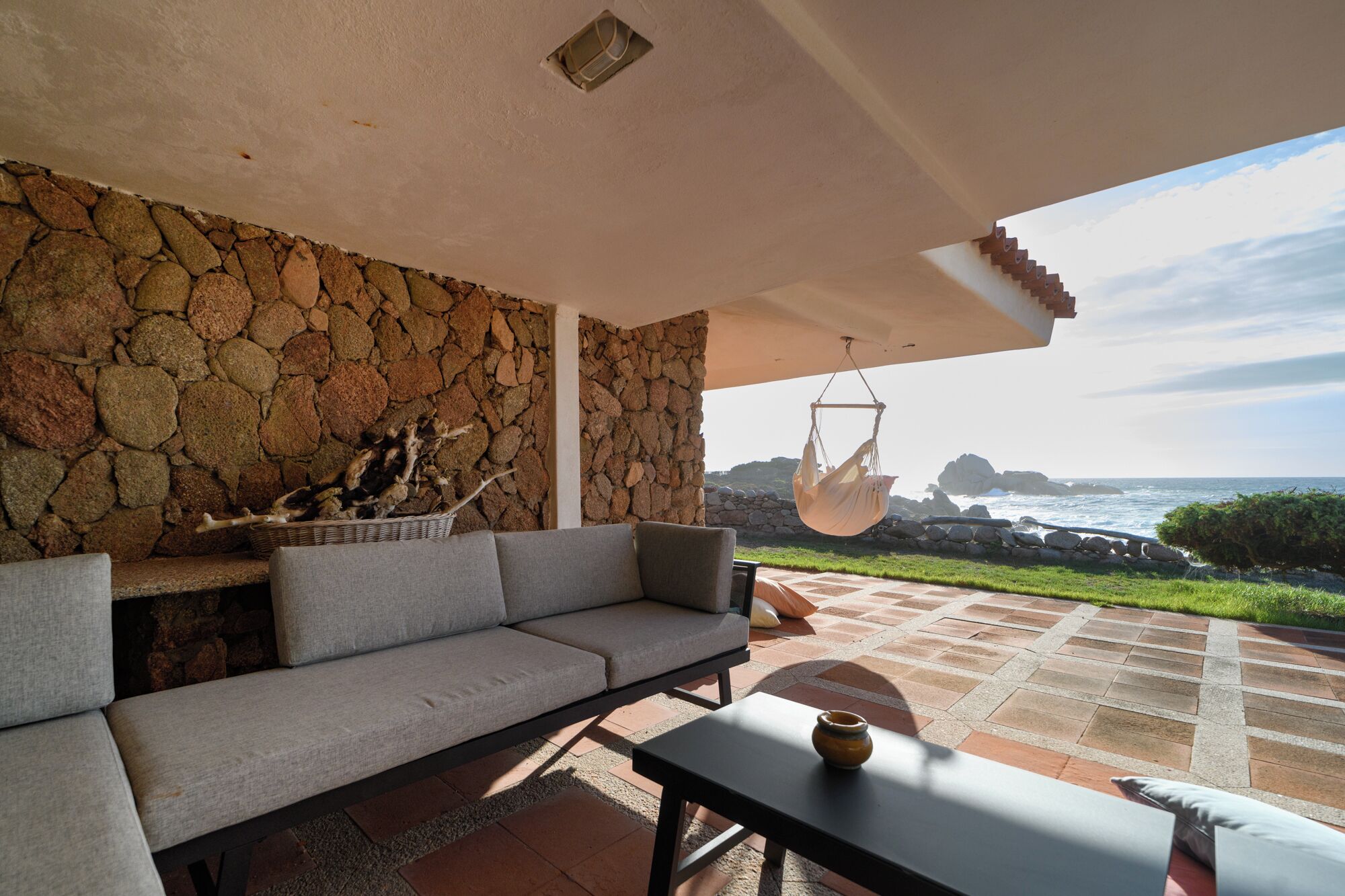 A stone wall, a sofa, a hanging chair, and a view of the ocean.