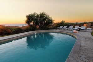 A swimming pool with lounge chairs, surrounded by greenery and a view of the sea at sunset. - Villa Portobello 10+2, Emma Villas (Portobello)