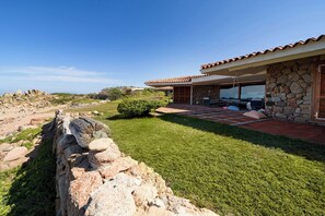 A modern house with a stone facade, a patio with outdoor furniture, and a view of a rocky landscape. - Villa Portobello 10+2, Emma Villas (Portobello)