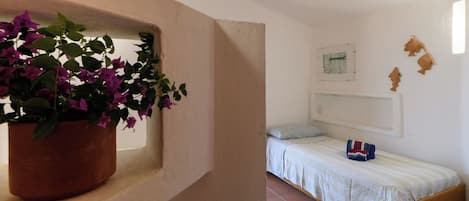 Un dormitorio con una cama, una ventana con una planta en maceta y una estantería de pared.