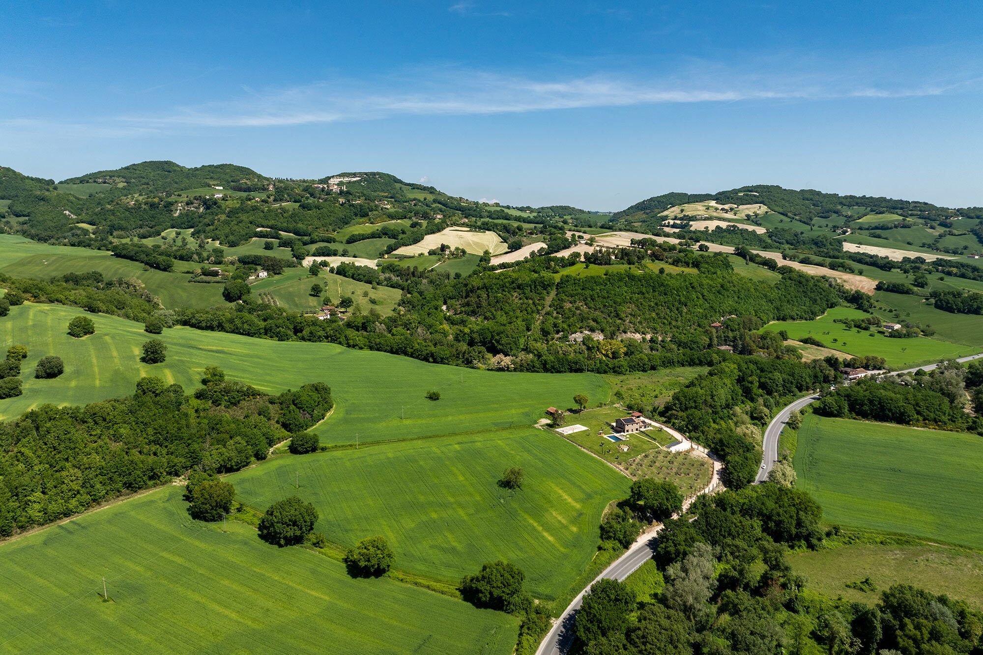 Vista aérea de un paisaje rural con colinas onduladas, campos verdes y edificios dispersos.