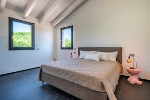 Ein Schlafzimmer mit einem großen Bett, zwei Fenstern, einem Nachttisch und einem auffälligen rosafarbenen Beistelltisch.