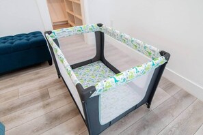 A baby playpen with a patterned cover, a dark blue sofa, and wooden flooring. - 12BR Luxury Home | Hot Tub | Ideal for Groups (Austin)
