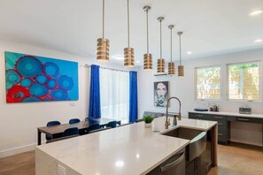 Une cuisine moderne dotée d’un îlot central, de luminaires suspendus et d’un grand tableau abstrait accroché au mur.