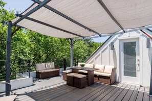 An outdoor patio with a covered seating area, a table, and a door leading to an interior space. - 12BR Luxury Home | Hot Tub | Ideal for Groups (Austin)