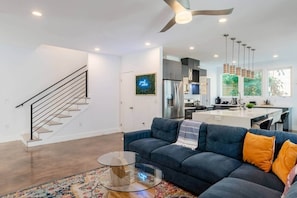Ein modernes Wohnzimmer mit einem blauen Sofa, einem Glastisch und einer Treppe.