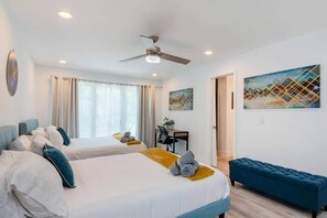 A hotel room with two beds, a desk, a blue sofa, and artwork on the walls. - 12BR Luxury Home | Hot Tub | Ideal for Groups (Austin)