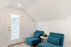 Ein Zimmer mit einer weißen Tür, einem kleinen runden Tisch mit einer Pflanze und zwei blauen Stühlen.