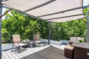 Eine Terrassenauslauf mit überdachter Sitzecke, Metallgeländern und Blick auf üppiges Grün.