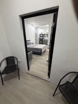 A room with a bed, a desk, a chair, and a kitchenette area.